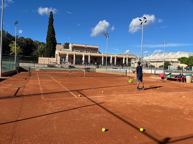Outdoor clay tennis court with multiple tennis balls on it.